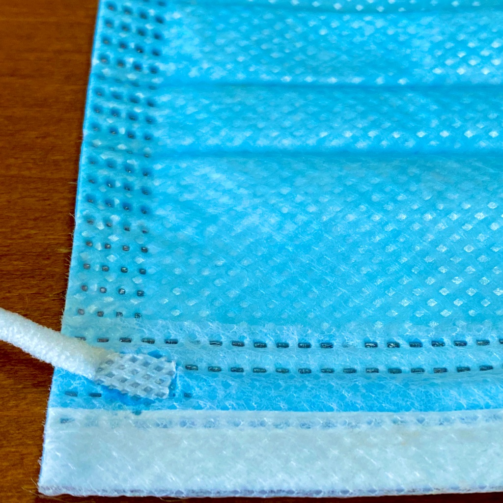 Zoomed in view of a surgical mask illustrating the stitching that links three distinct layers.